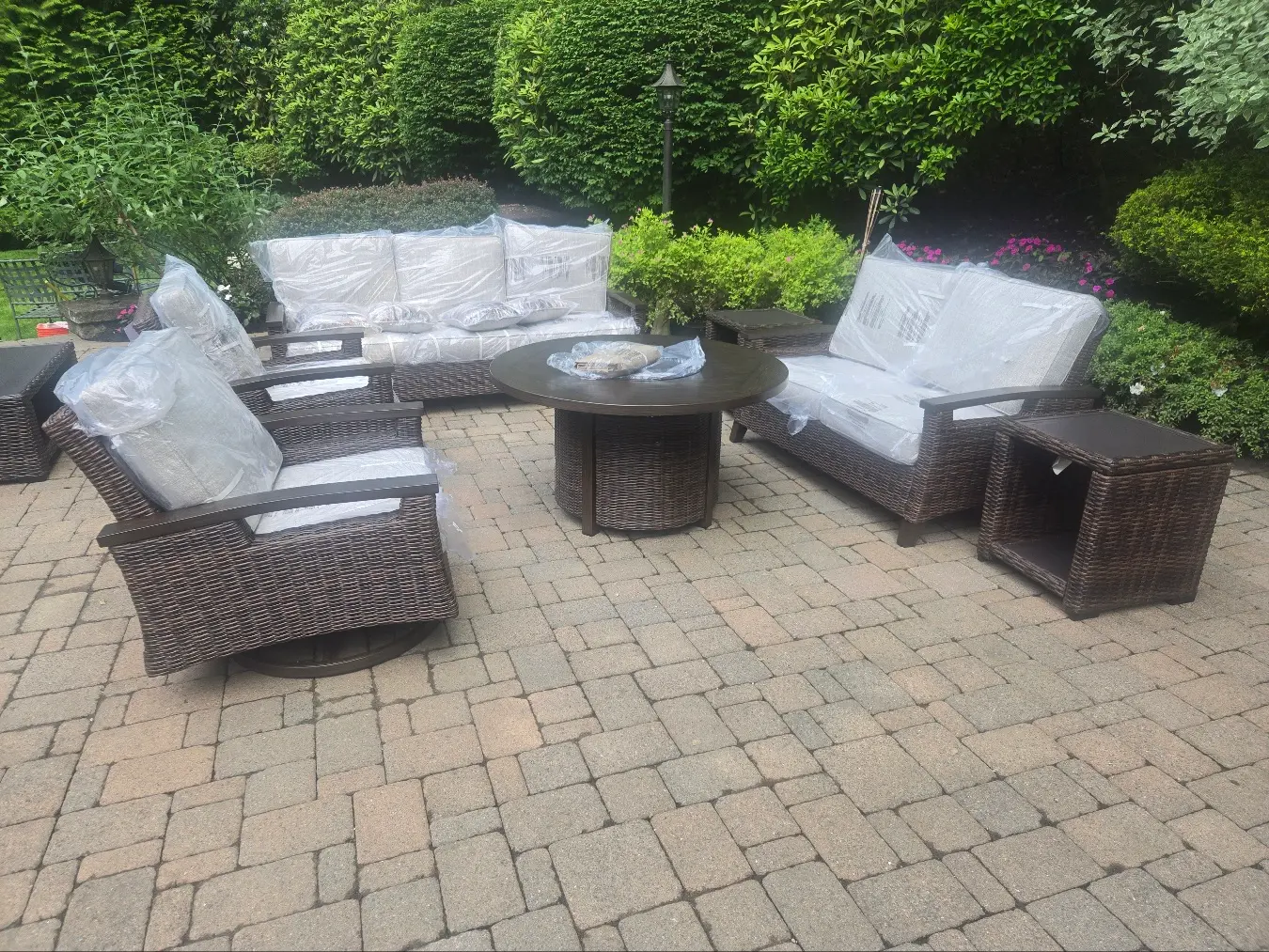 Patio set with three-cushion couch, love seat, two arm chairs, circular table with fire pit, and end table on customer’s patio delivered by RF Delivery